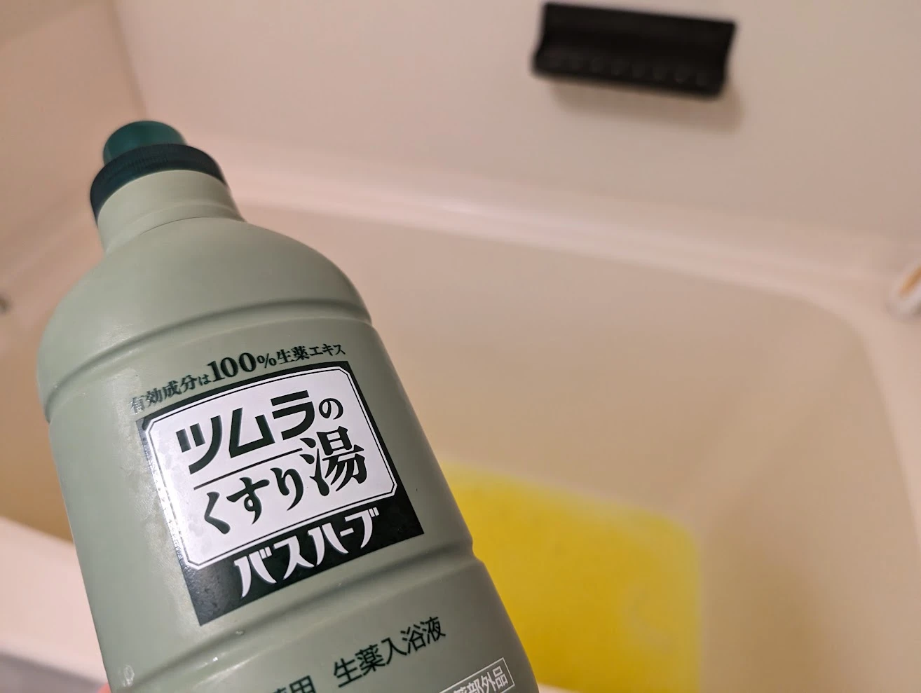 ツムラのくすり湯バスハーブのボトルと、黄色い湯を張っている浴槽